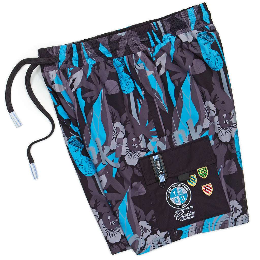 Front view of Cookies Corsica Black Swim Shorts on a wooden deck against a tropical backdrop, showcasing the sleek and stylish design with a comfortable fit for all-day wear