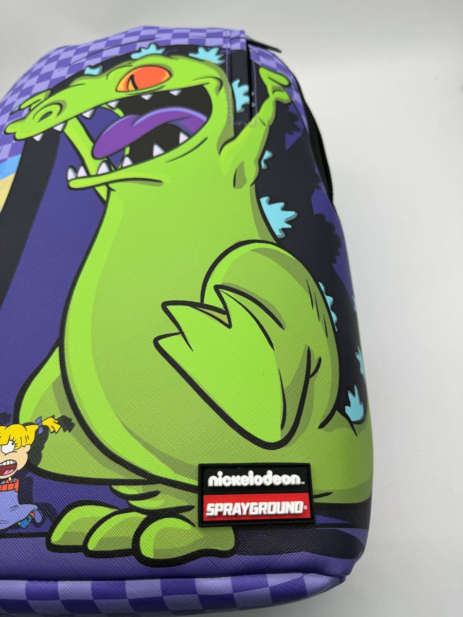 Front view of the Sprayground Reptar Chase Backpack showcasing its 18-inch height, 115-inch width, and 65-inch depth with vibrant graphics