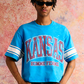 Cropped blue tee with varsity stripe sleeves and bold KANSAS print on front