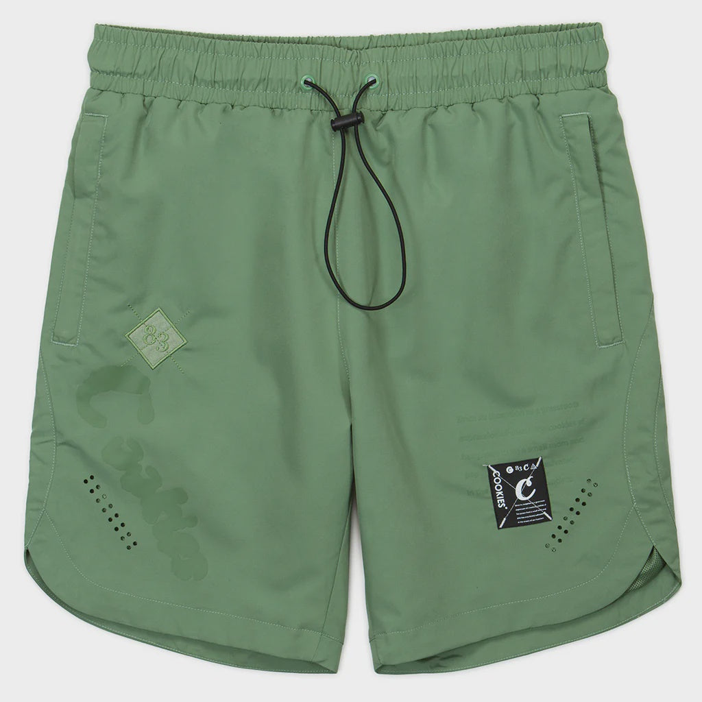Close-up of Cookies Key Largo Light Olive Swim Shorts on sandy beach with waves in background, perfect for summer vacation and beach activities